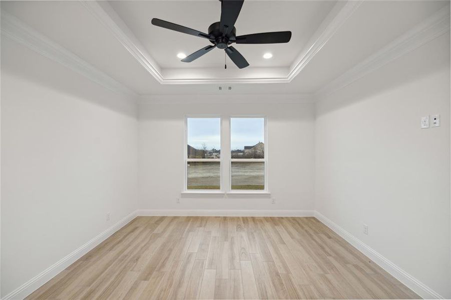 Empty room with ceiling fan, light wood-type flooring, crown molding, and a tray ceiling