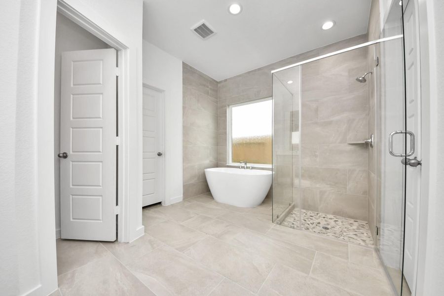 Escape to a spa-like oasis in this primary bathroom. Enjoy a walk-in shower with tile surround, a separate garden tub with custom detailing, and an elegant vanity featuring light countertops, modern hardware, and beautiful recessed lights. Experience luxury and relaxation in every detail. Sample photo of completed home with similar floor plan. Actual colors and selections may vary.