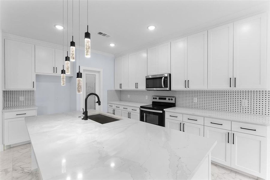 Kitchen with white cabinets, appliances with stainless steel finishes, light stone countertops, and sink