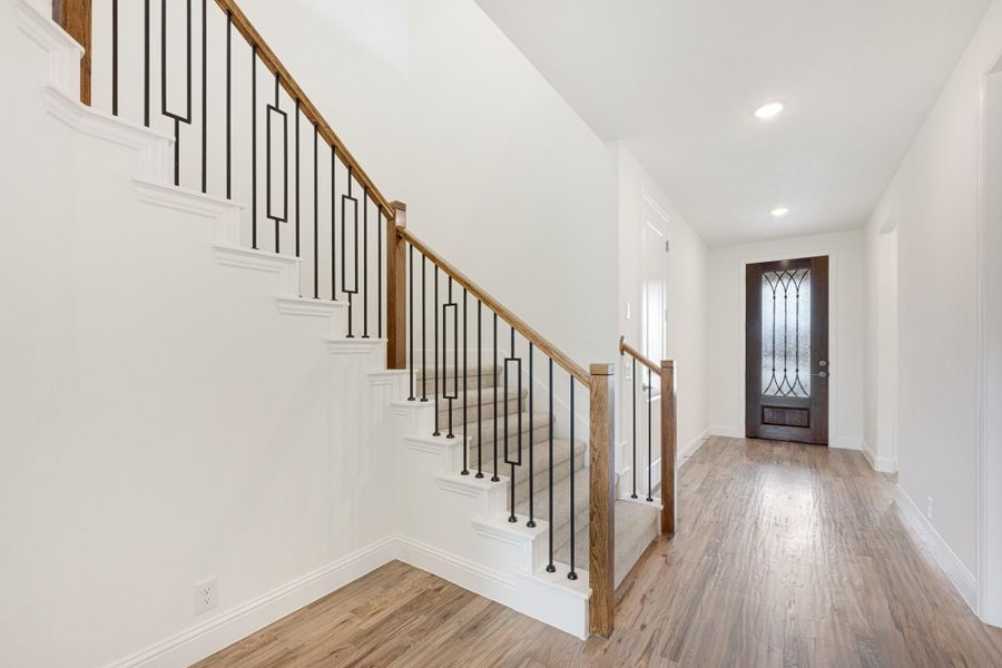 Entryway with staircase featuring wood handrail and black iron balusters, hardwood floors, and wood front door with glass panel Entryway with staircase featuring wood handrail and black iron balusters, hardwood floors, and wood front door with glass panel