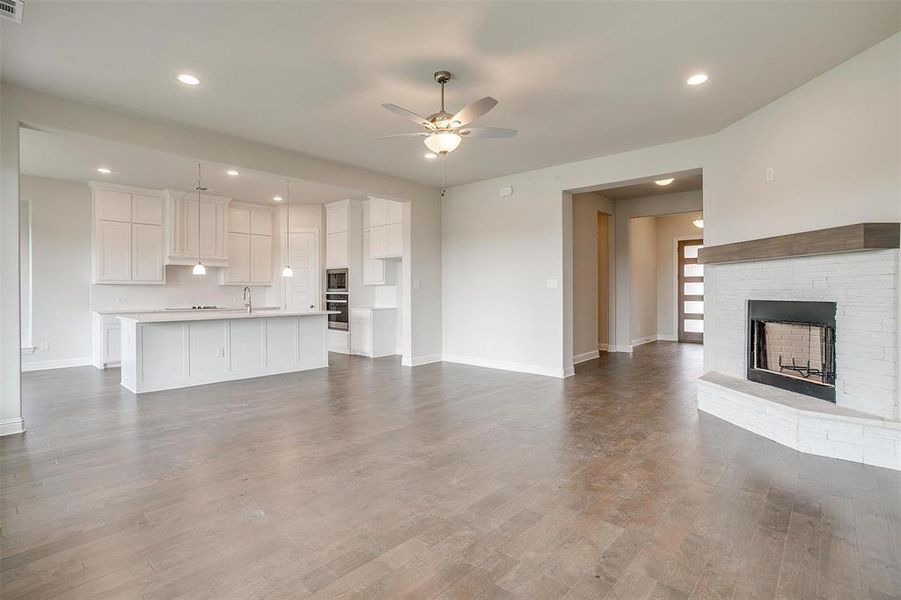 Unfurnished living room with ceiling fan, wood-type flooring, sink, and a brick fireplace