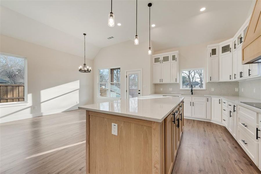 Kitchen featuring white cabinetry, a center island, glass insert cabinets, hanging light fixtures, and vaulted ceiling