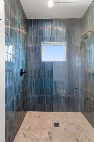 A striking walk-in shower features rich blue tile walls and a light-toned stone floor, illuminated by a high window.