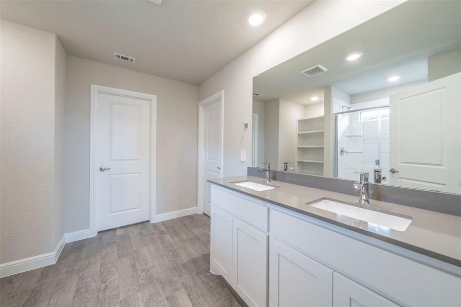 Bathroom featuring hardwood / wood-style floors, a shower with door, and two sinks.  Door straight on is the walk in closet.  Door on the right is the toilet.