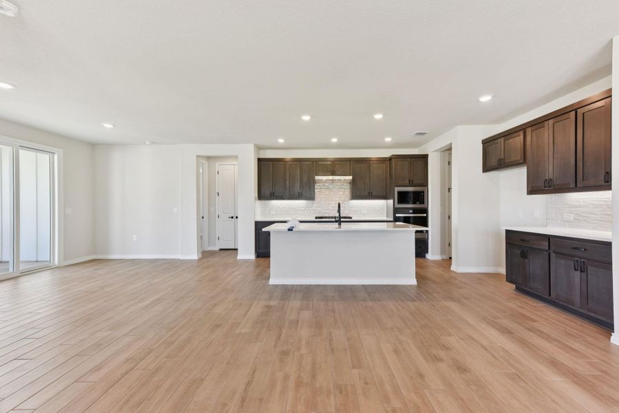 Kitchen with dark brown cabinetry, recessed lighting, light wood-style flooring, stainless steel microwave, and open floor plan