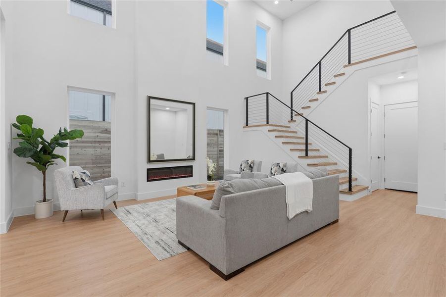 Living room featuring a glass covered fireplace, light wood-style floors, plenty of natural light, recessed lighting, and a high ceiling