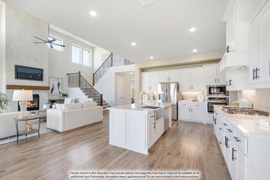 Open-concept kitchen with white cabinets and island flowing into living room with fireplace and staircase