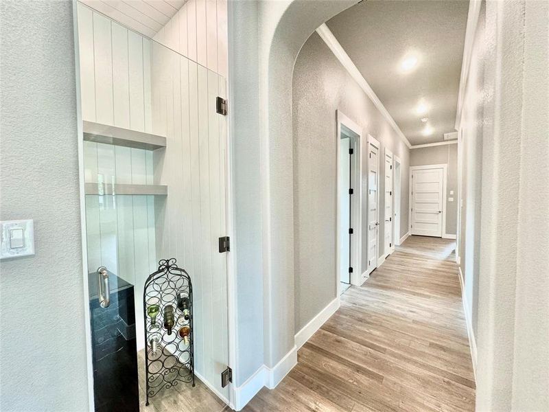 Hallway with arched walkways, a textured wall, light wood-style flooring, crown molding, and baseboards