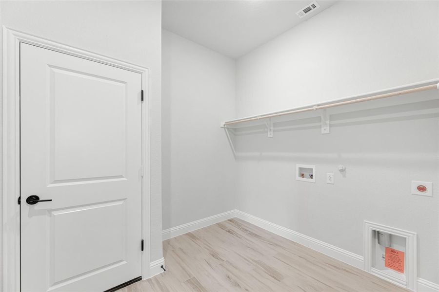 Laundry room with wall-mounted shelf, washer and dryer hookups, and light wood-look floors Laundry room with wall-mounted shelf, washer and dryer hookups, and light wood-look floors