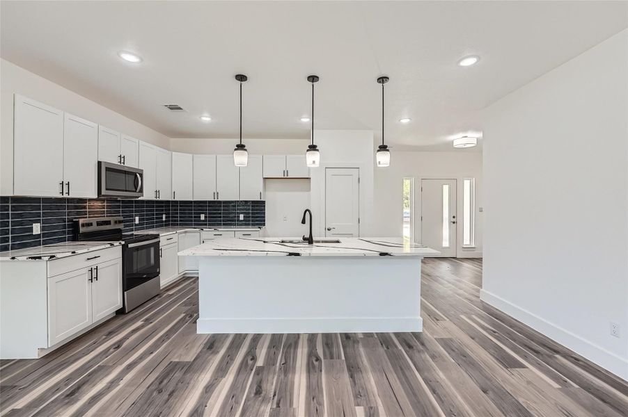 Kitchen with appliances with stainless steel finishes, backsplash, recessed lighting, and an island with sink