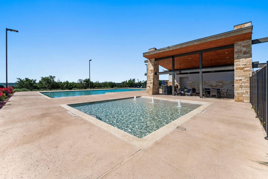 Outdoor amenity space featuring two distinct pools, a stone-clad covered pavilion with exposed wood-finish ceiling, a textured concrete deck, and perimeter landscaping