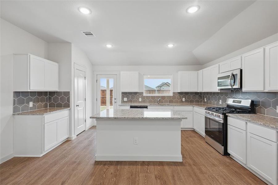 Kitchen with vaulted ceiling, stainless steel appliances, a center island, and light wood finished floors Kitchen with vaulted ceiling, stainless steel appliances, a center island, and light wood finished floors