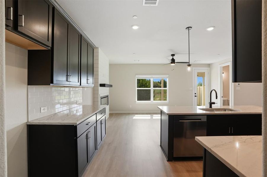 Kitchen with light stone countertops, stainless steel dishwasher, backsplash, light wood finished floors, and a ceiling fan Kitchen with light stone countertops, stainless steel dishwasher, backsplash, light wood finished floors, and a ceiling fan