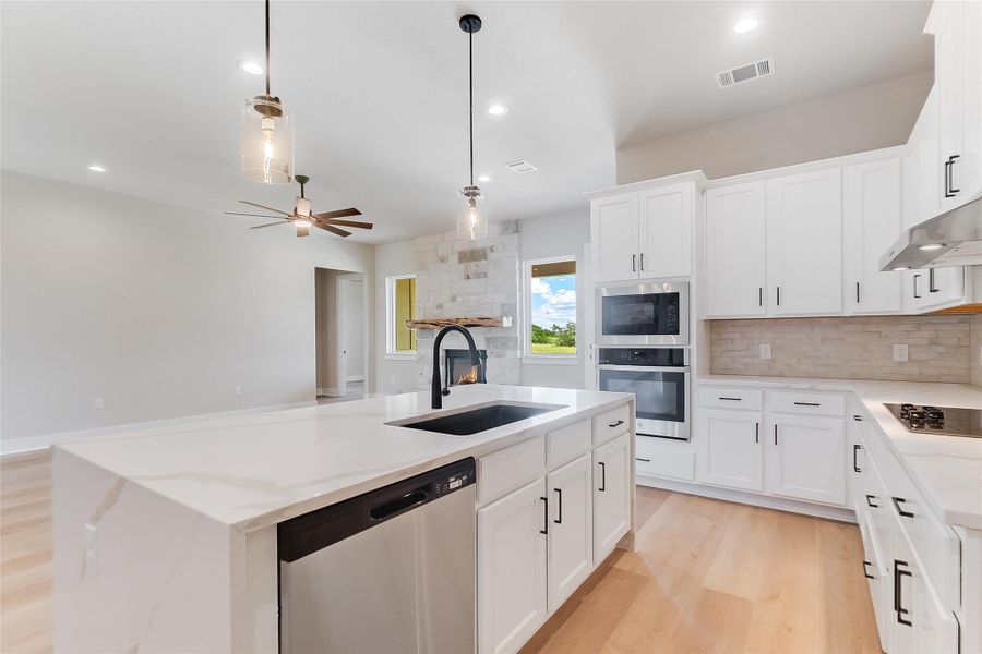 Kitchen with stainless steel appliances, white cabinets, a kitchen island with sink, light wood-style flooring, and hanging light fixtures