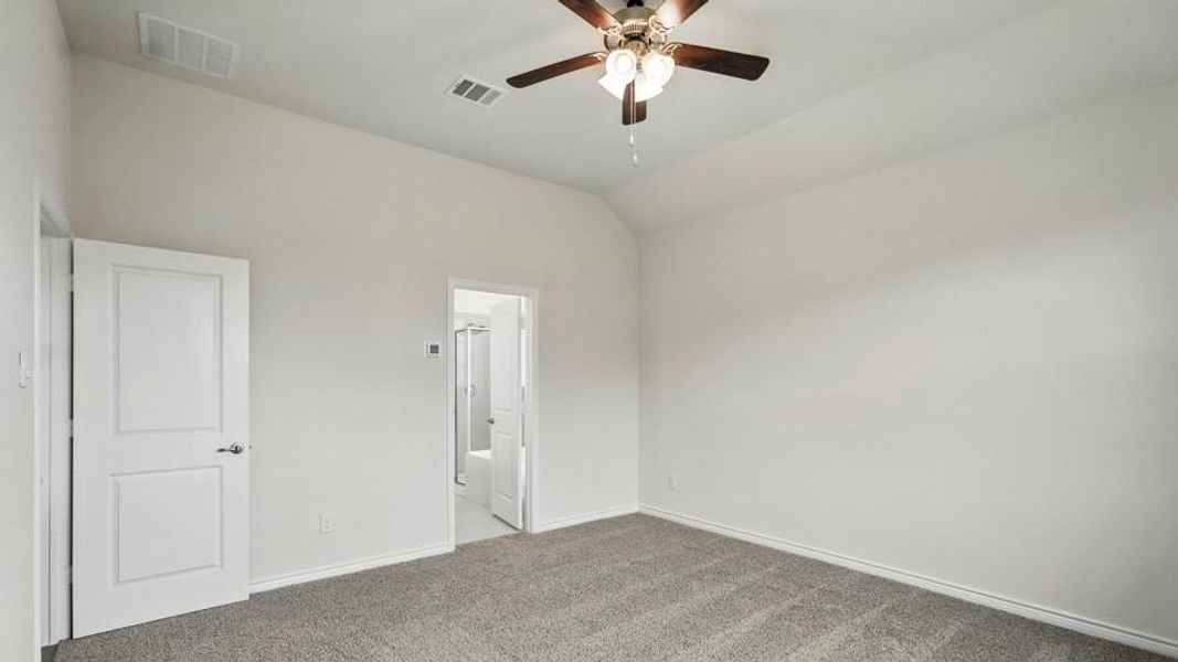 Spacious interior room featuring vaulted ceilings, a ceiling fan with integrated lighting, and neutral grey carpet flooring