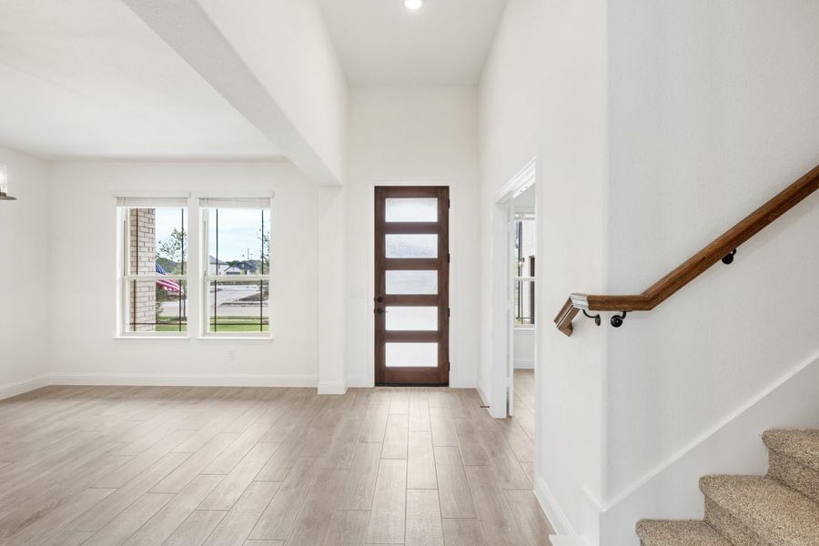 Open entryway with dark wood front door, light wood floors, high ceilings, and staircase with wood railing