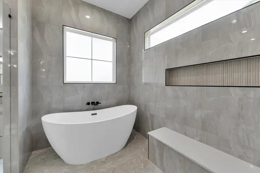 This elegant bathroom features a freestanding tub, glass-enclosed shower, and modern fixtures. It has large tiles, a spacious layout, and ample natural light from a frosted window, offering a serene and luxurious feel.