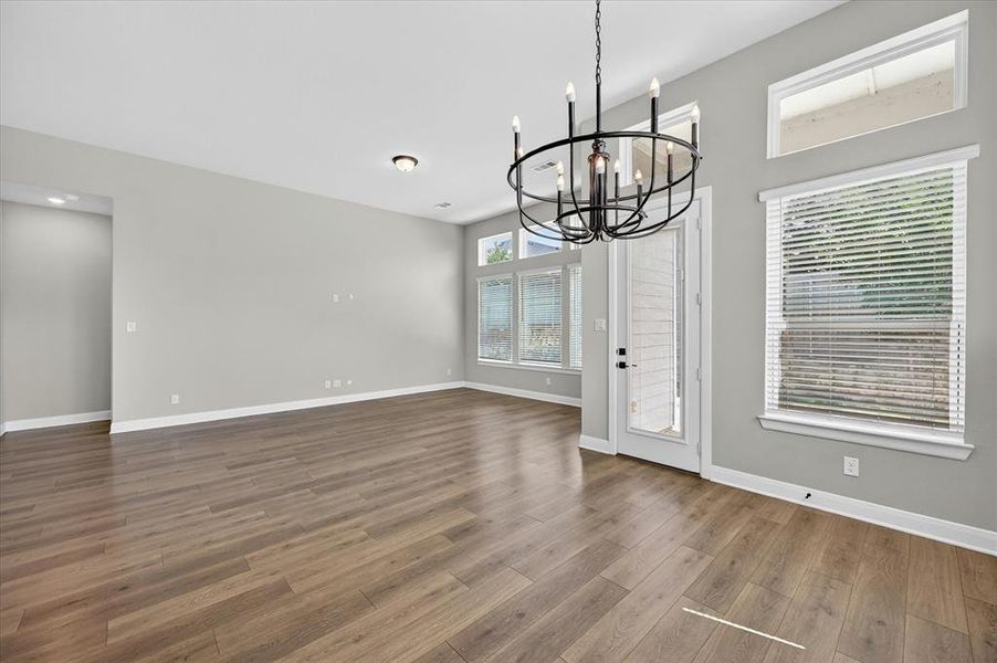 Open-concept living area featuring wood-finish flooring, a contemporary chandelier, multiple windows with blinds, a glass-panel door, and recessed lighting Open-concept living area featuring wood-finish flooring, a contemporary chandelier, multiple windows with blinds, a glass-panel door, and recessed lighting