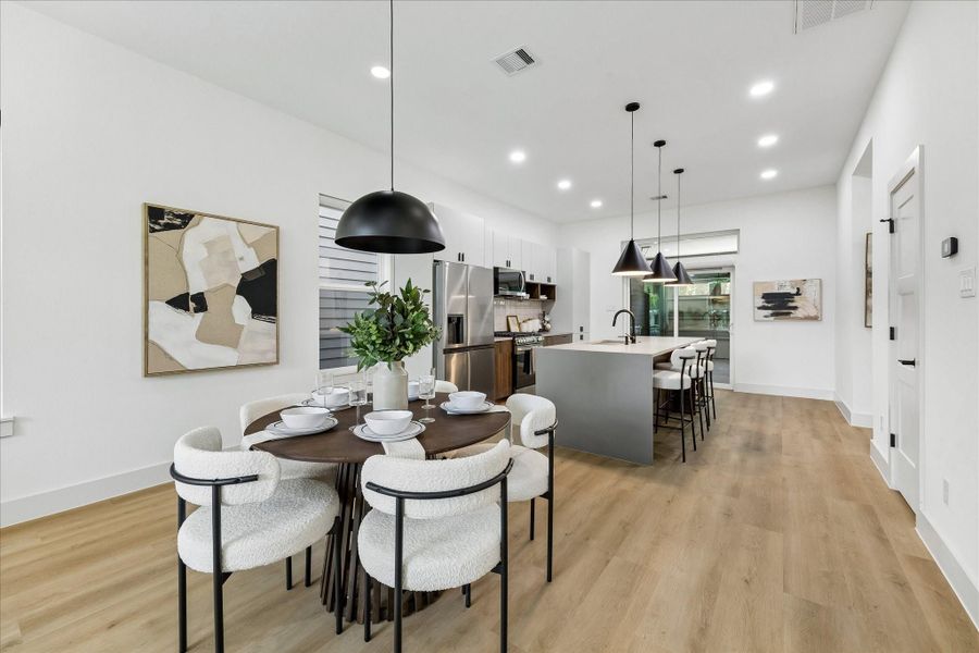 Oversized black statement pendants anchor the dining space while expansive windows and warm contemporary finishes create an inviting atmosphere for everyday meals and entertaining.