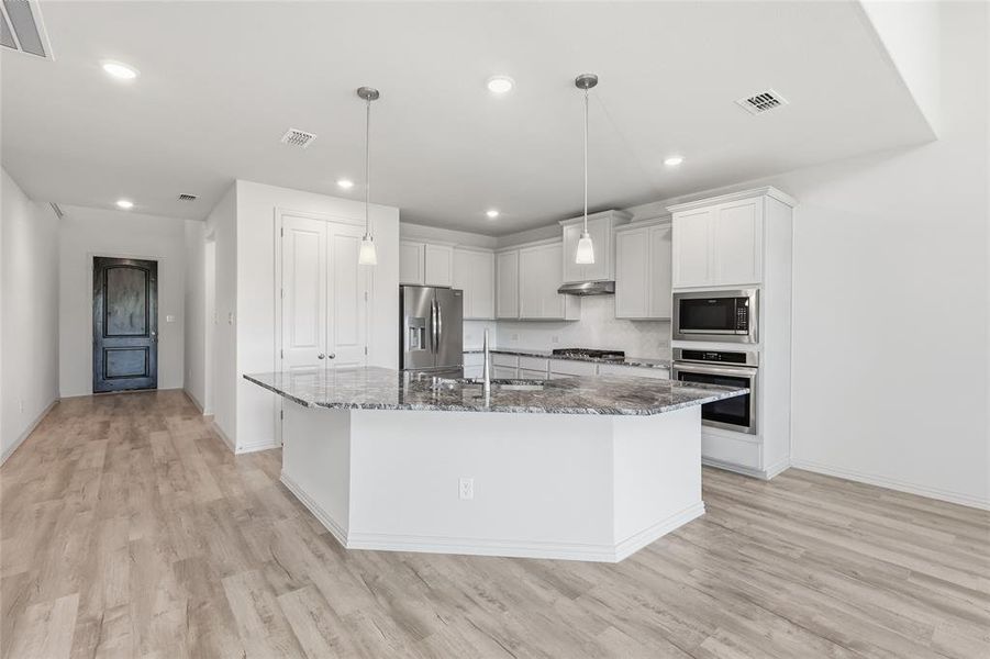 Kitchen with dark stone counters, stainless steel appliances, a kitchen island with sink, white cabinetry, and light wood-style flooring Kitchen with dark stone counters, stainless steel appliances, a kitchen island with sink, white cabinetry, and light wood-style flooring