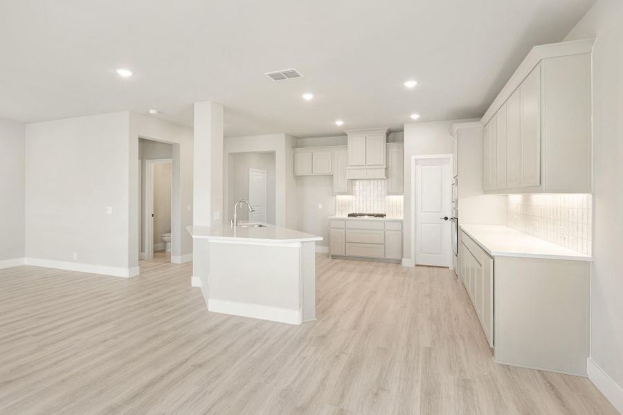 Open kitchen with center island, gray cabinets, white countertops, tile backsplash, and light wood floors