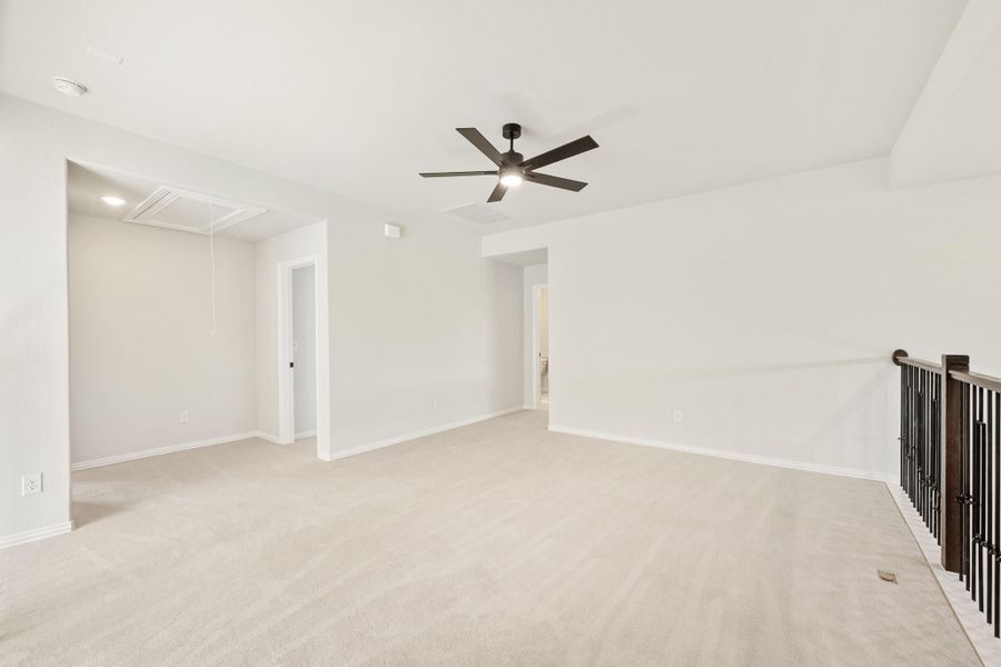 Open upstairs loft with beige carpet, ceiling fan, and stair railing along the right wall