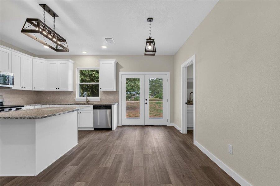 Double glass doors open to the outdoors from this bright, open kitchen space with wood-style flooring. Double glass doors open to the outdoors from this bright, open kitchen space with wood-style flooring.
