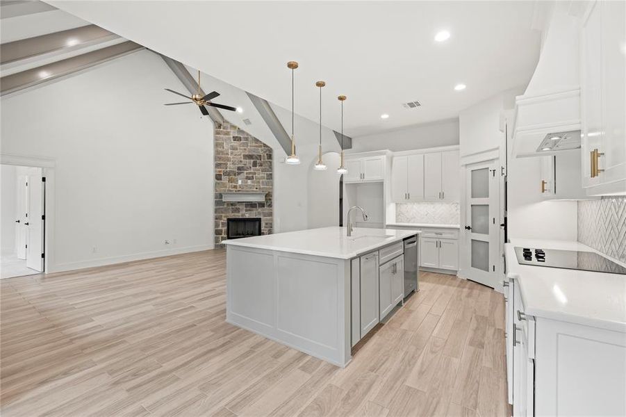 Kitchen with white cabinets, light wood-type flooring, hanging light fixtures, tasteful backsplash, and a fireplace