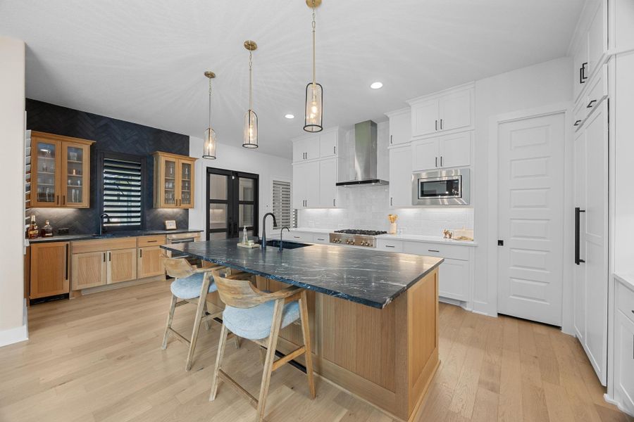 Kitchen with a kitchen island with sink, glass insert cabinets, light wood-style floors, a kitchen breakfast bar, and recessed lighting