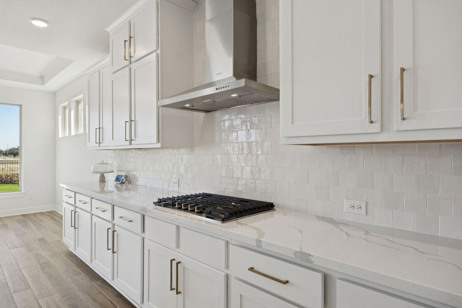 A built-in gas cooktop is seamlessly integrated into the countertops and set beneath a professional stainless steel vent hood, combining style and functionality. A built-in gas cooktop is seamlessly integrated into the countertops and set beneath a professional stainless steel vent hood, combining style and functionality.