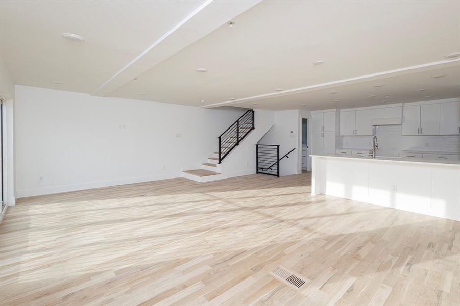 Unfurnished living room with light wood finished floors, baseboards, visible vents, stairway, and a sink