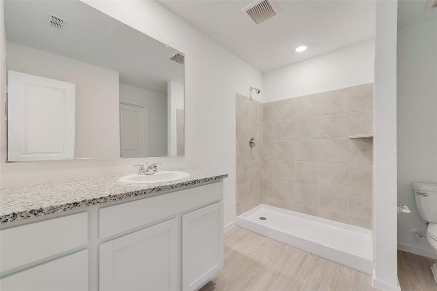 Bathroom featuring vanity, wood-type flooring, toilet, and tiled shower