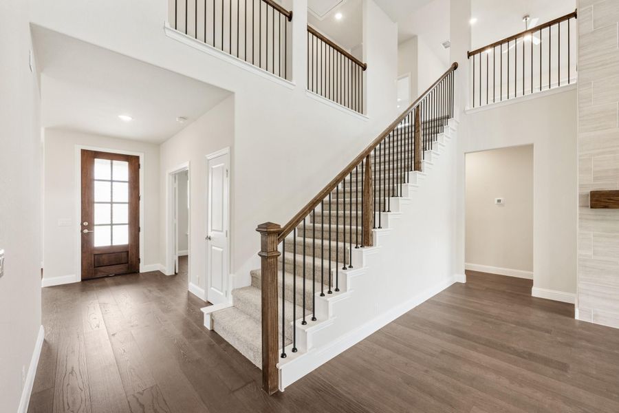 Two-story foyer with carpeted staircase, wood and iron railing, hardwood floors, and glass-panel front door