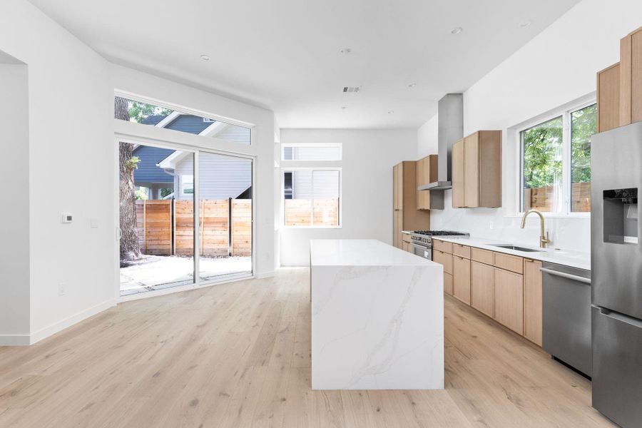 Kitchen with modern cabinets, stainless steel appliances, a kitchen island, light stone counters, and light wood-style flooring Kitchen with modern cabinets, stainless steel appliances, a kitchen island, light stone counters, and light wood-style flooring
