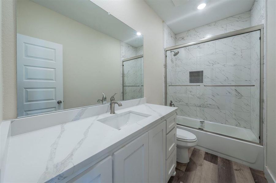 Full bath with bath / shower combo with glass door, vanity, wood finished floors, and toilet