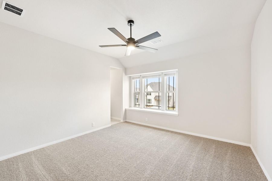 Empty bedroom with vaulted ceiling, ceiling fan, carpet flooring, and large window Empty bedroom with vaulted ceiling, ceiling fan, carpet flooring, and large window