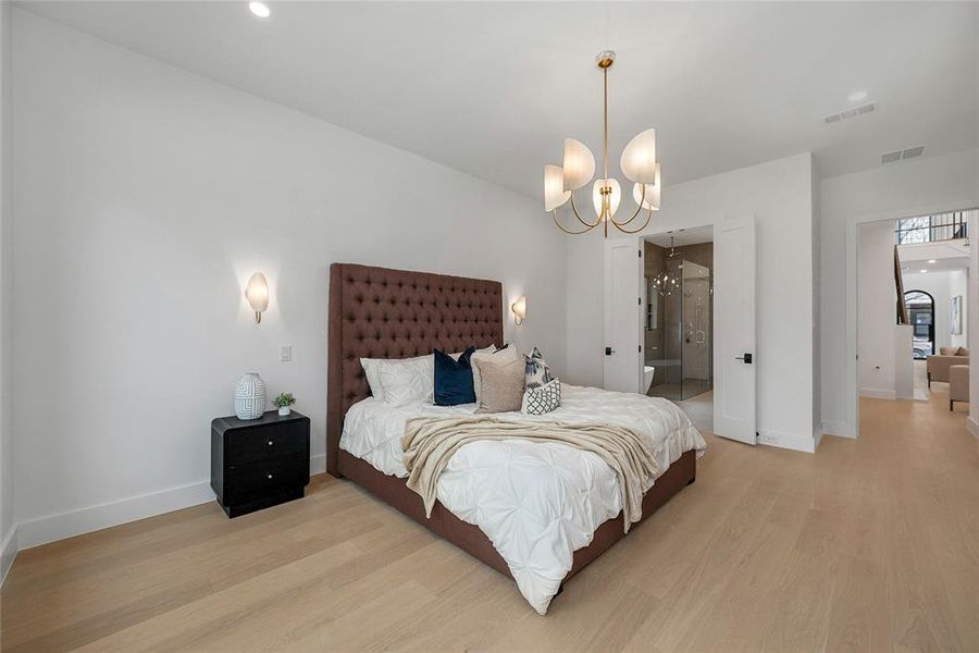 Bedroom featuring light wood-style flooring, suspended lighting, and ensuite bathroom Bedroom featuring light wood-style flooring, suspended lighting, and ensuite bathroom