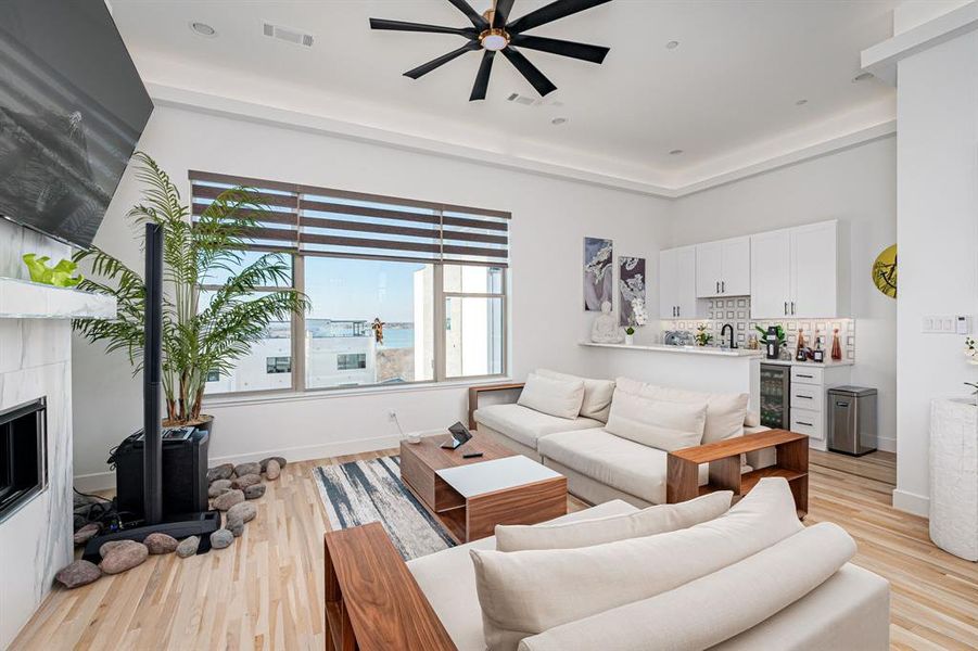 Living room with ceiling fan, sink, a fireplace, light hardwood / wood-style floors, and wine cooler