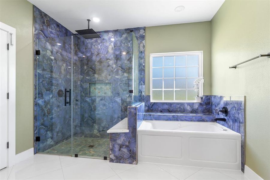 This bathroom features a luxurious design with a spacious glass-enclosed shower, stunning blue stone tile accents, and a large soaking tub. Natural light pours in through a frosted window, enhancing the serene atmosphere.