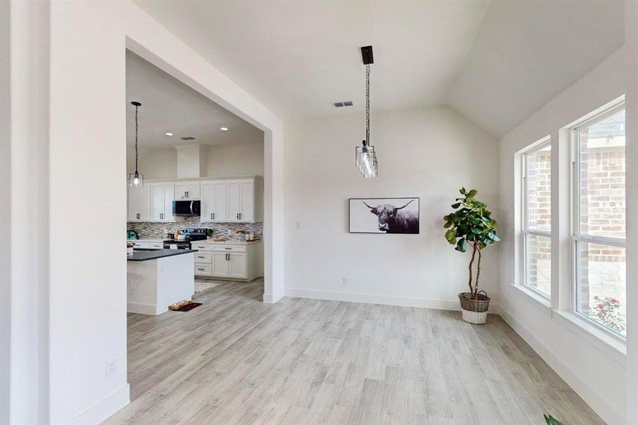 Kitchen with tasteful backsplash, stainless steel appliances, decorative light fixtures, light hardwood / wood-style flooring, and white cabinets