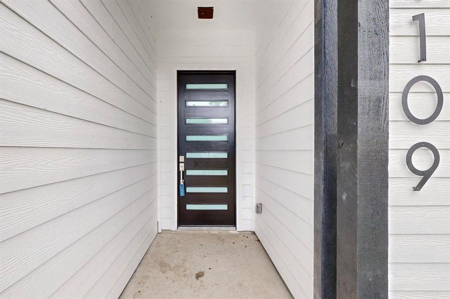Modern entry featuring horizontal siding, a contemporary dark wood-finish door with frosted glass panels, and distinct house numbers Modern entry featuring horizontal siding, a contemporary dark wood-finish door with frosted glass panels, and distinct house numbers