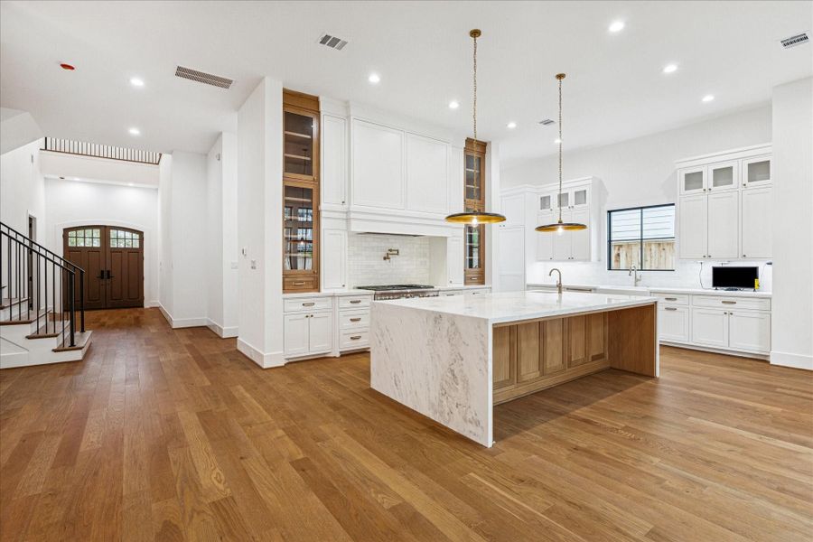 A dramatic marble waterfall island anchors the kitchen, offering an impressive workspace framed by warm oak accents and brass details. Custom cabinetry rises to the ceiling, blending inset paneling with glass-front displays to showcase the craftsmanship Arch Angelo is known for. The vent hood surround becomes architectural art, and the pot filler over the range adds both function and refinement. Pre plumbing for water softener systems and future Generac integration supports long term value and reliability. A dramatic marble waterfall island anchors the kitchen, offering an impressive workspace framed by warm oak accents and brass details. Custom cabinetry rises to the ceiling, blending inset paneling with glass-front displays to showcase the craftsmanship Arch Angelo is known for. The vent hood surround becomes architectural art, and the pot filler over the range adds both function and refinement. Pre plumbing for water softener systems and future Generac integration supports long term value and reliability.