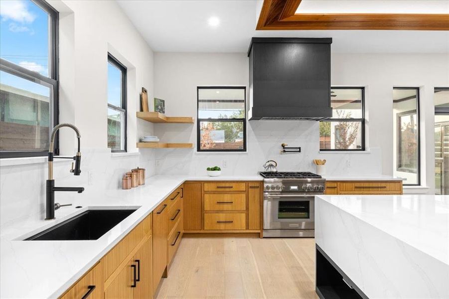 Kitchen with custom exhaust hood, sink, double oven range, light hardwood / wood-style flooring, and backsplash