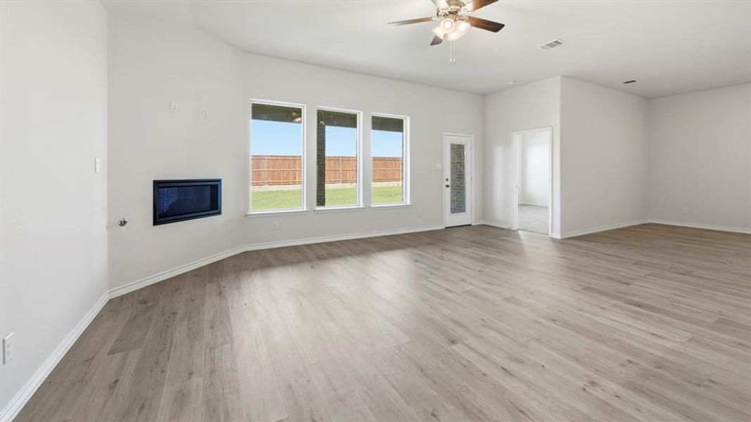 Unfurnished living room with light wood-style flooring, ceiling fan, and a glass covered fireplace Unfurnished living room with light wood-style flooring, ceiling fan, and a glass covered fireplace