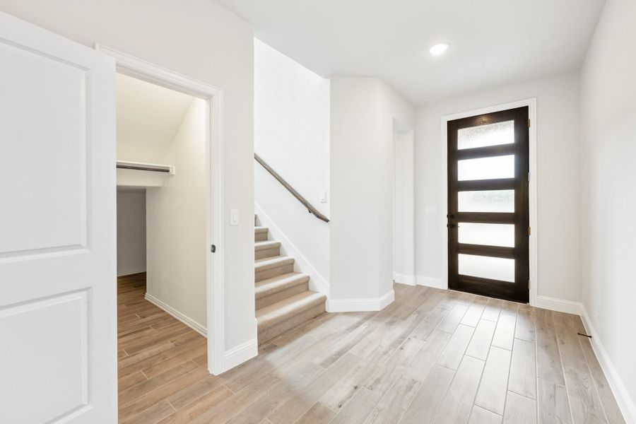 Entryway with dark front door, staircase, wood-look floors, and open closet with white walls