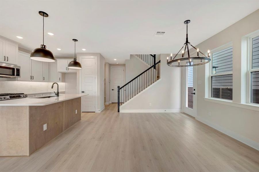 Kitchen featuring a chandelier, light wood-type flooring, a kitchen island with sink, and white cabinetry