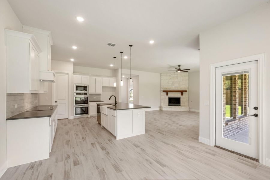 Open-concept kitchen with white cabinets, center island, and living area with stone fireplace visible beyond.