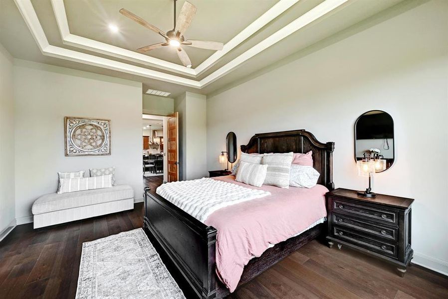 Bedroom featuring a tray ceiling, a ceiling fan, dark wood finished floors, and connected bathroom