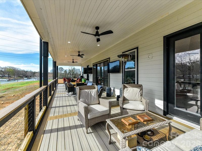 Expansive covered balcony featuring multiple seating areas, ceiling fans, and scenic water views perfect for outdoor entertaining.