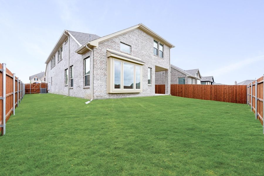 Two-story brick home with large windows and spacious fenced backyard with green lawn